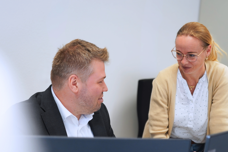 Zwei Mitarbeitende arbeiten gemeinsam hinter zwei Monitoren.