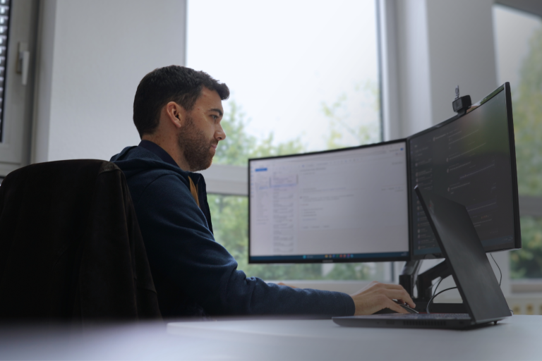 Person arbeitet fokussiert an zwei Monitoren, Symbol für datenanalytische Arbeit, technisches Know-how und präzise Umsetzung digitaler Strategien.